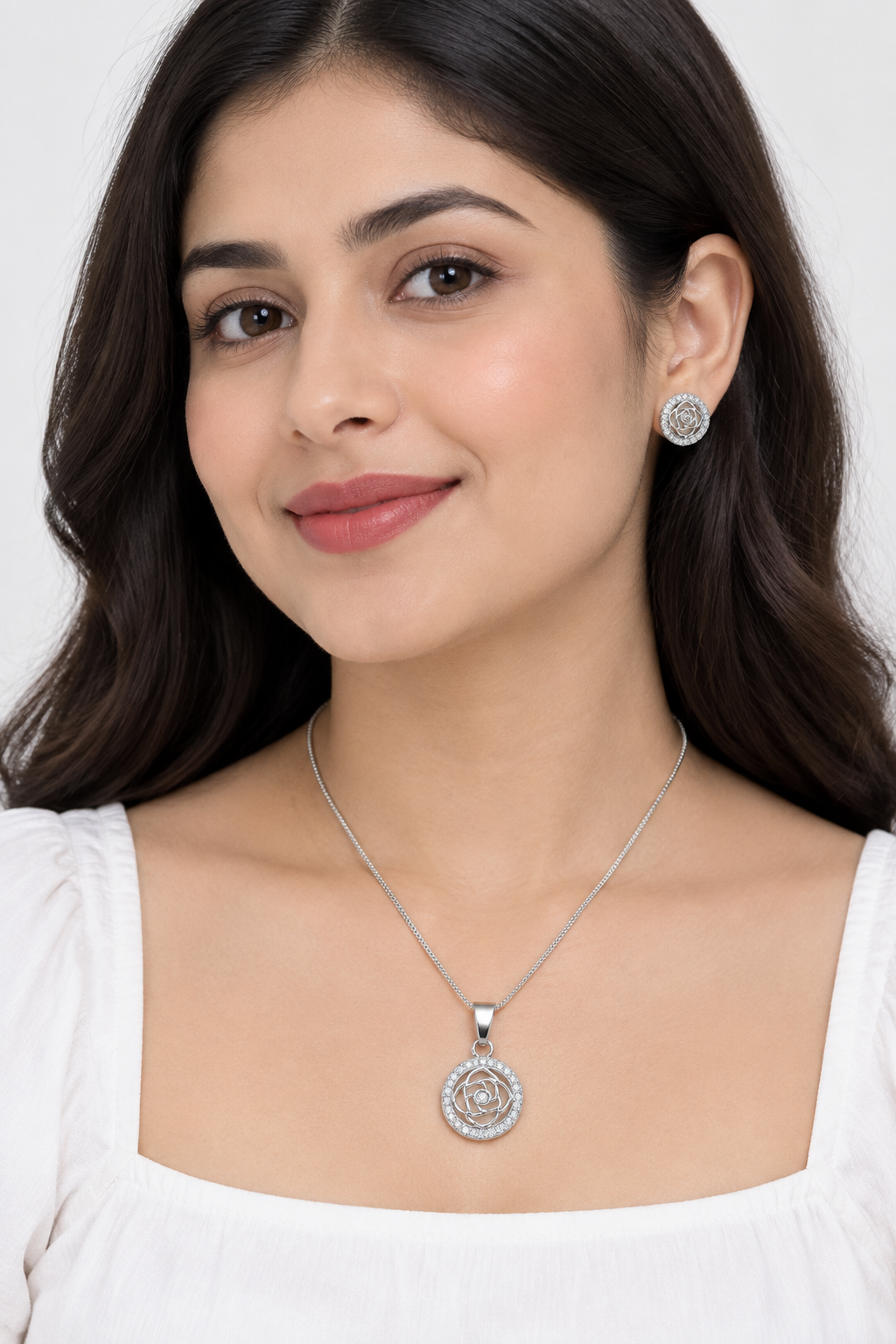 Styled model in white wearing silver-tone rose pendant necklace and round stud earrings