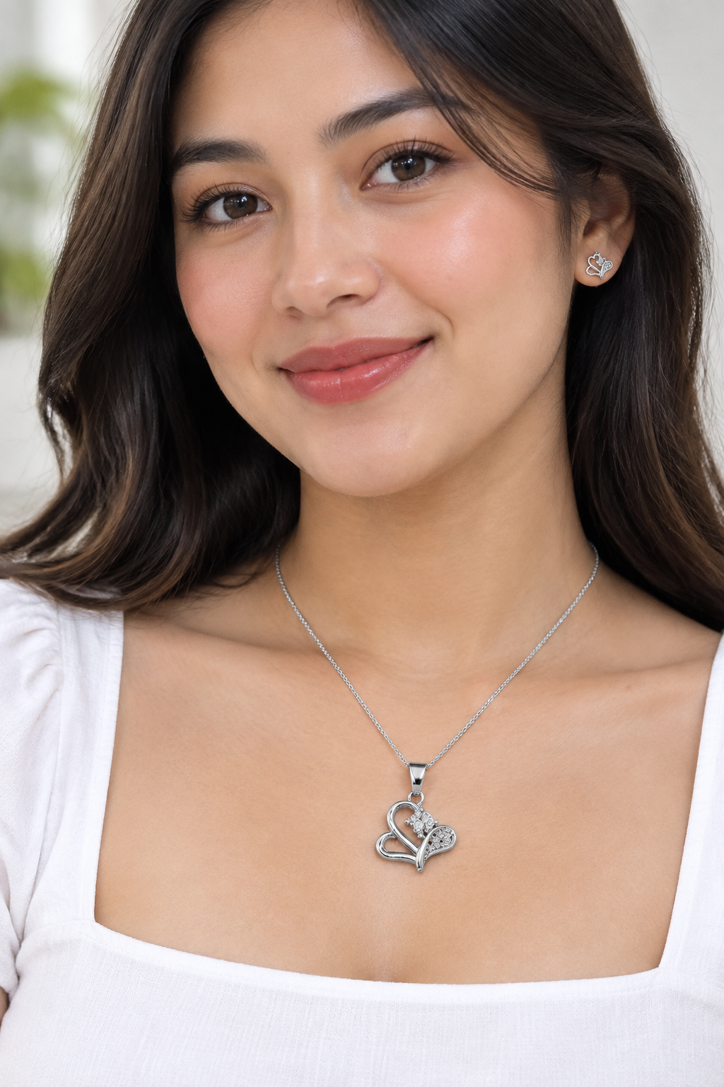 Styled model in white wearing silver-tone heart pendant and matching stud earring