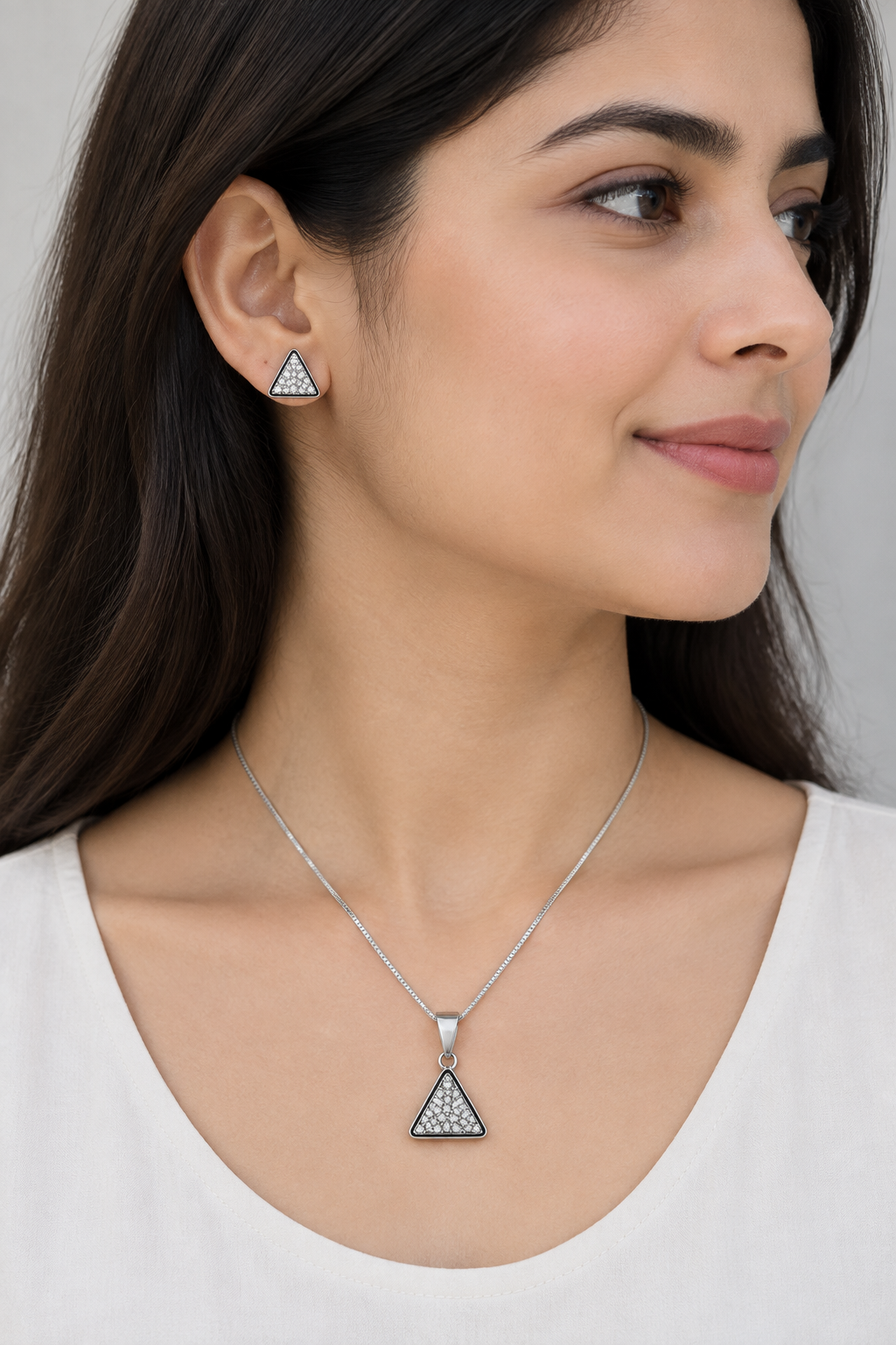 Styled model in white wearing silver-tone triangular pendant and matching stud earring