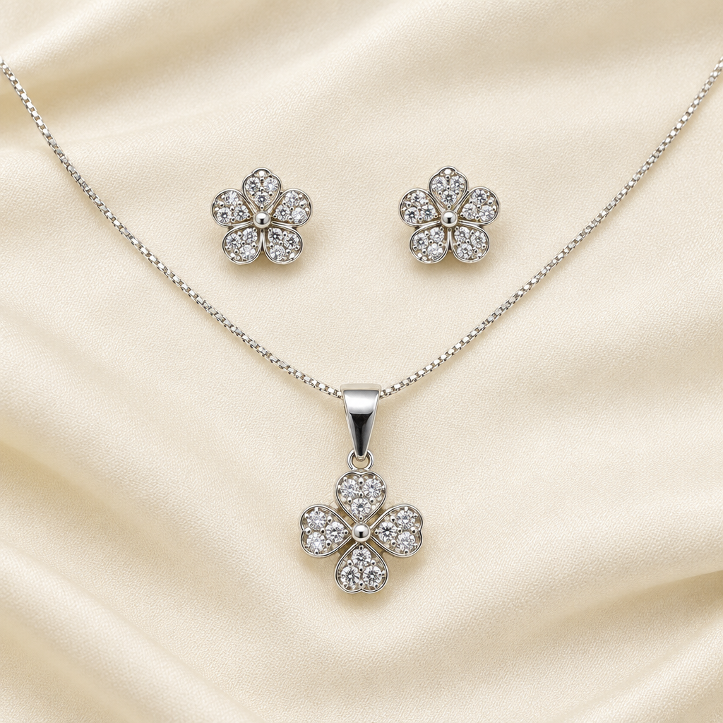 Matching silver-tone flower pendant and stud earrings laid on cream fabric
